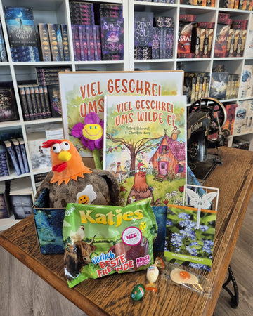 Das Produktbild zeigt vorn eine geöffnete Drachenpost in blauem Schuppen-Design. Man sieht das in den Boxdeckel geklebte Plakat zum Buch "Viel Geschrei ums wilde Ei", das Buch, unser Plüschhuhn Hilde und zum Thema passende Goodies - Süßigkeiten und andere Kleinigkeiten. Im Hintergrund sieht man die Bücherregale des Verlagsladens.